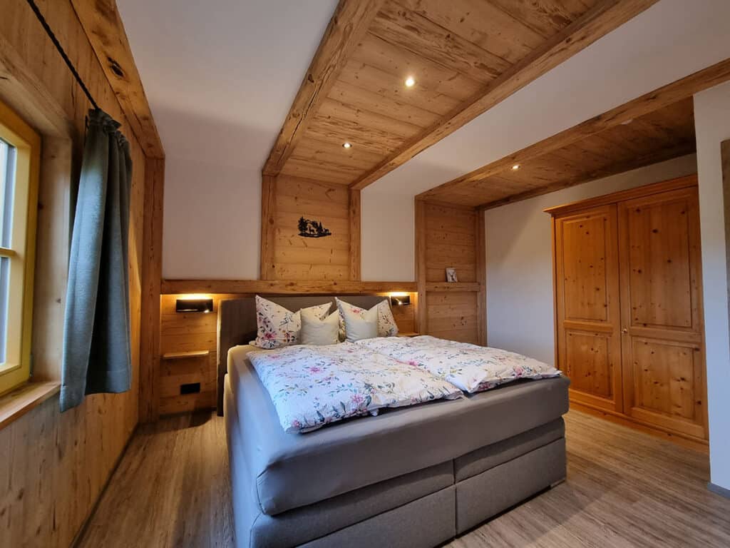 Schlafzimmer Nr.2 mit grauem Boxspringbett und Holzverkleidung_Alm Chalet